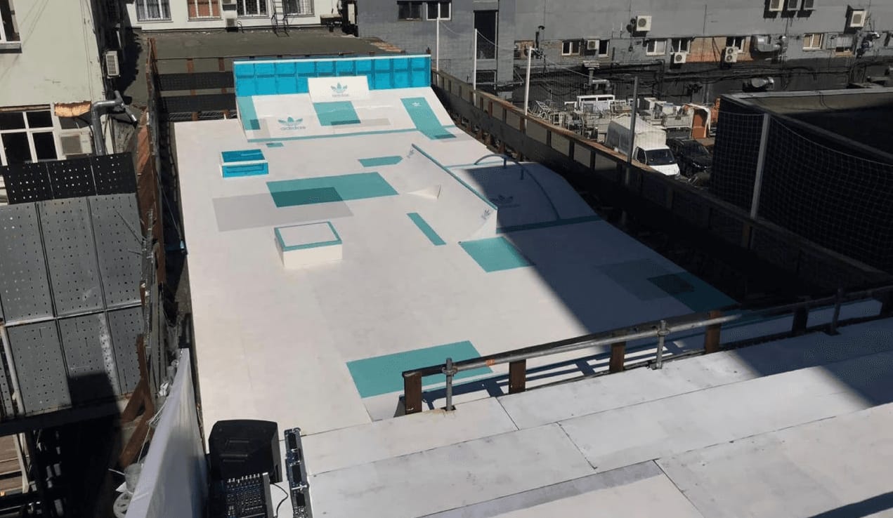 Adidas rooftop skatepark seen from above: white wooden ramps with turquoise graphics between city buildings
